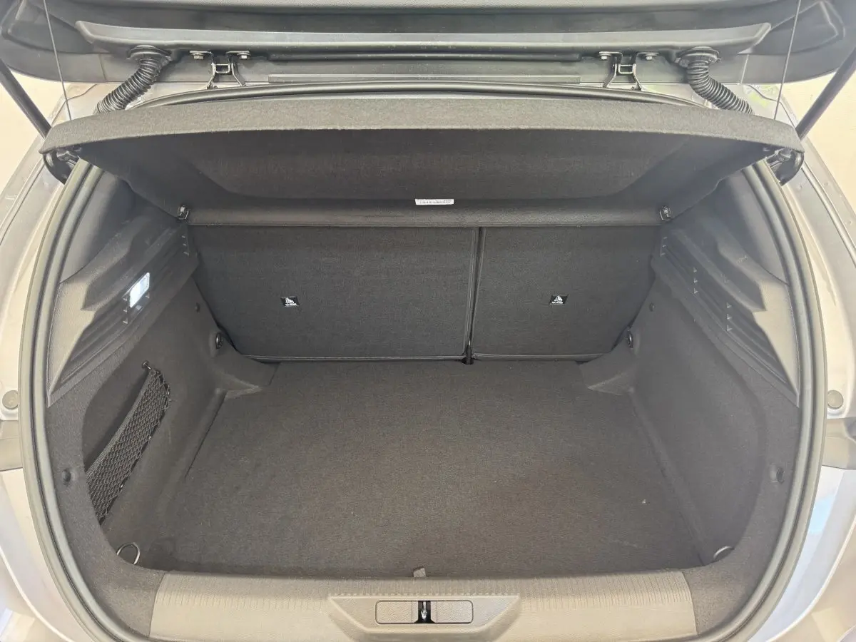 Vue intérieure du coffre ouvert de la Peugeot 308 gris clair, montrant l'espace de rangement et la banquette arrière rabattable.