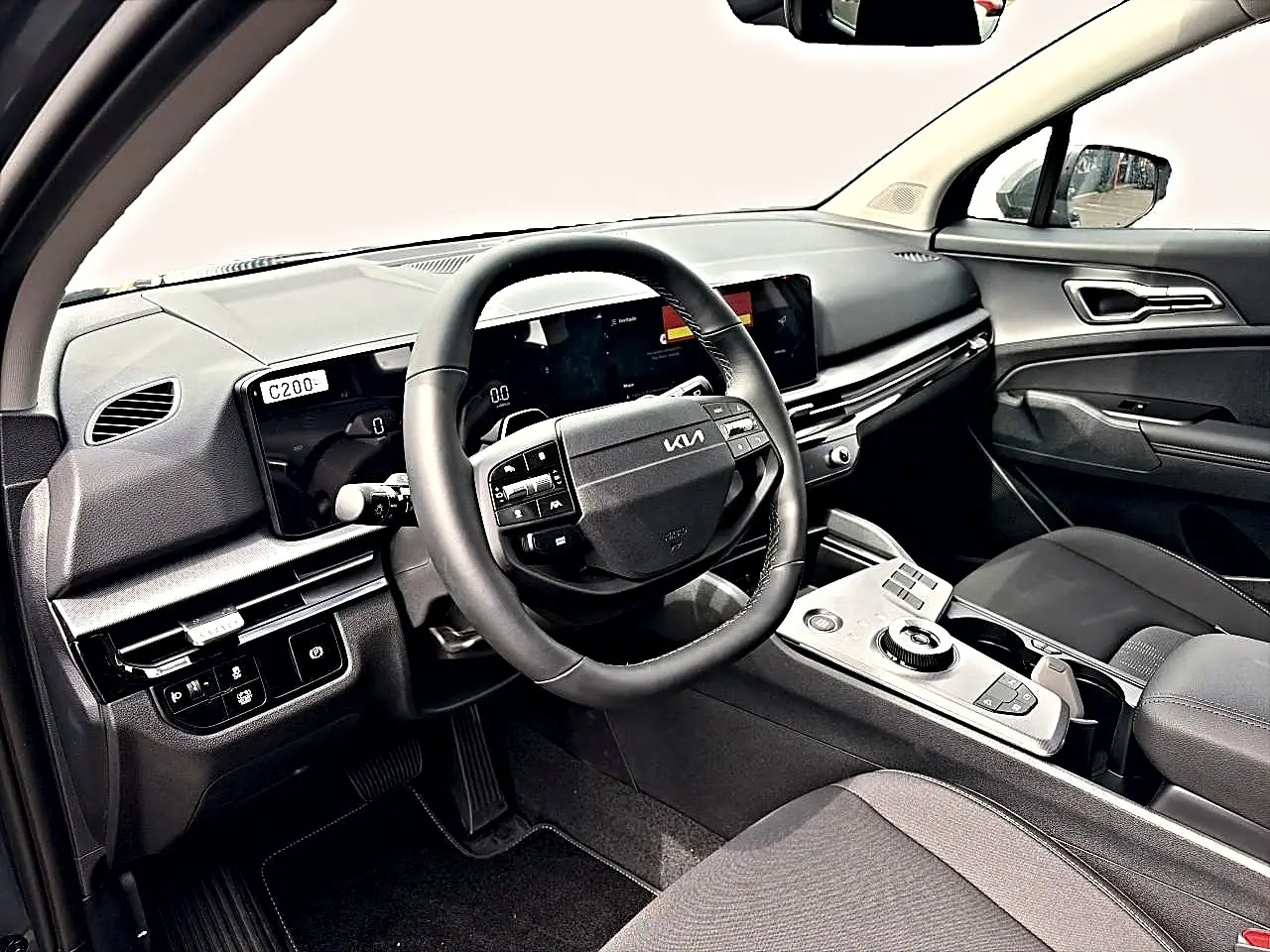 Vue intérieure côté conducteur du tableau de bord et volant cuir noir du Kia Sportage 1.6 hybride 239 gris eclipse.