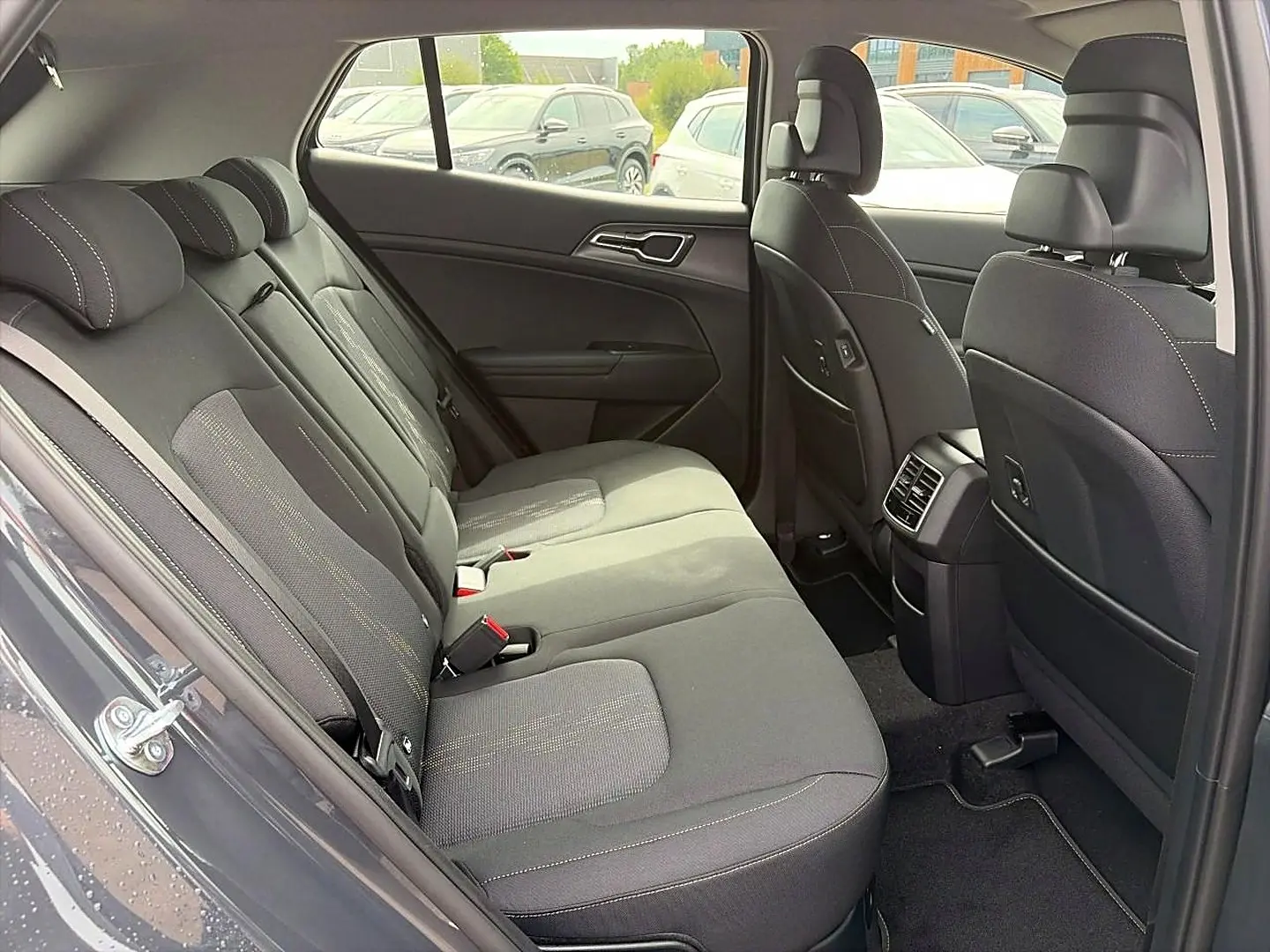 Vue intérieure côté gauche montrant la banquette arrière grise du Kia Sportage 1.6 hybride 239 active avec appuie-têtes et aérateurs centraux.
