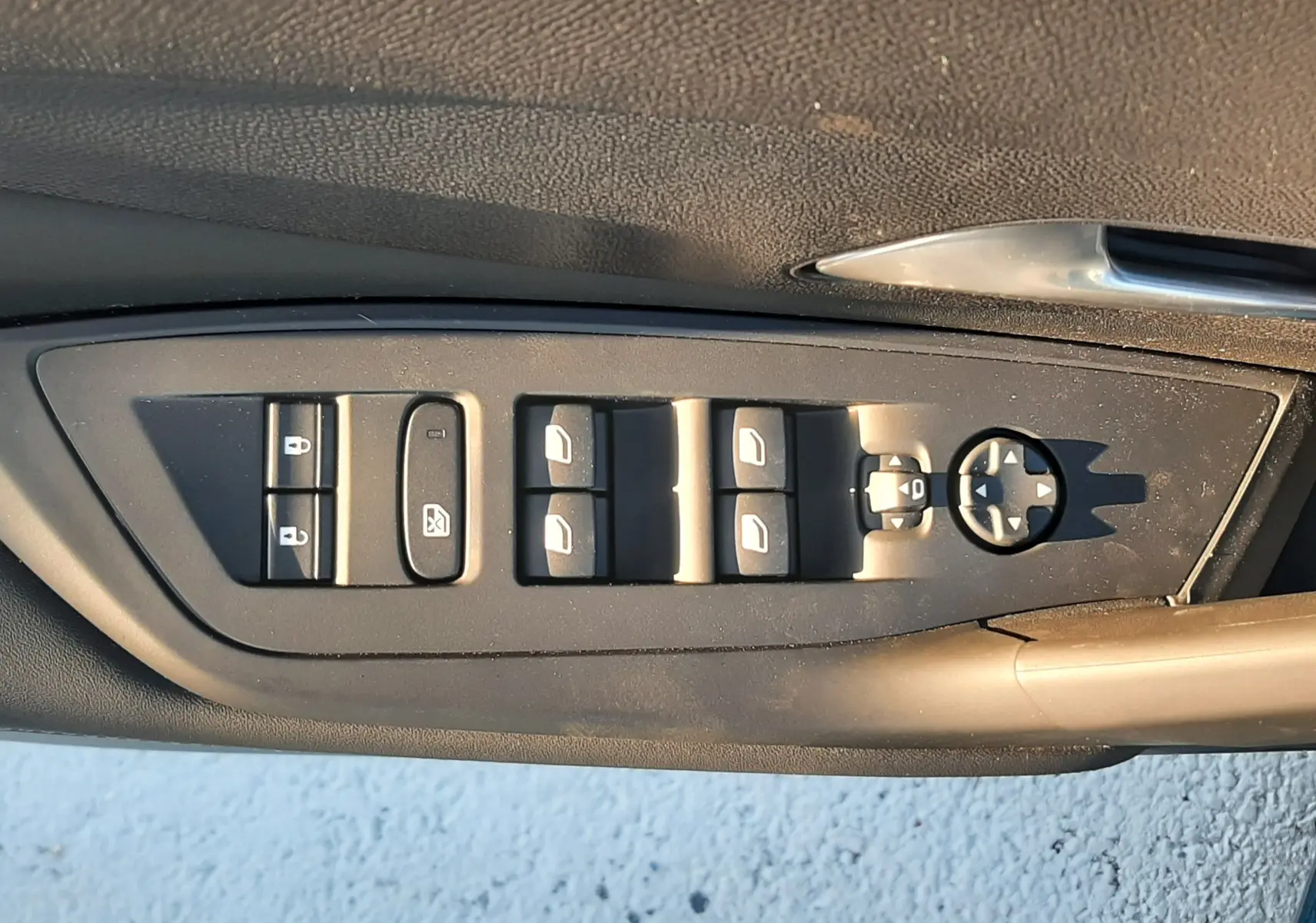 Vue rapprochée des commandes de lève-vitres et rétroviseurs sur la porte côté gauche d'une Peugeot 308 Bleu Obsession.