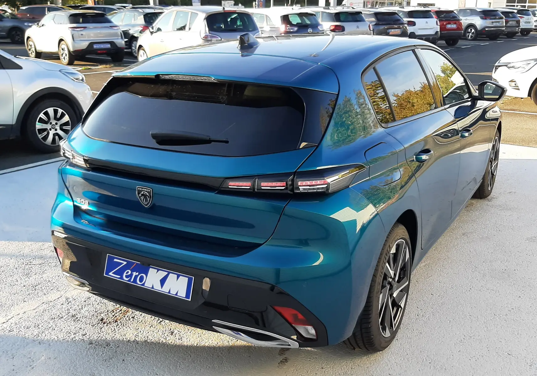 Vue 3/4 arrière droite d'une Peugeot 308 Bleu Obsession 2025 avec feux LED et vitres teintées sur parking.