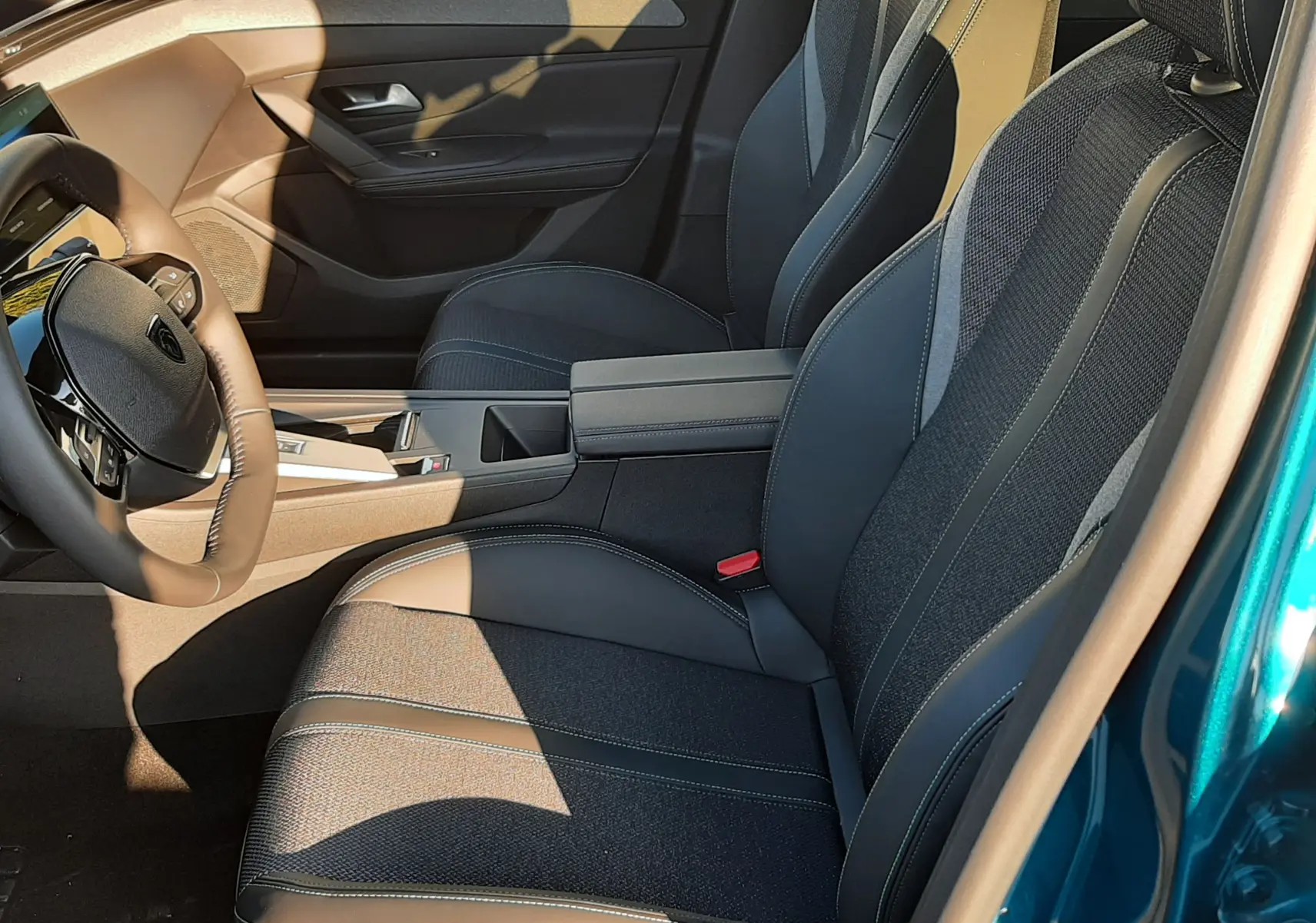 Vue intérieure côté conducteur de la Peugeot 308 2025 bleu obsession, sièges noirs avec surpiqûres claires et console centrale.