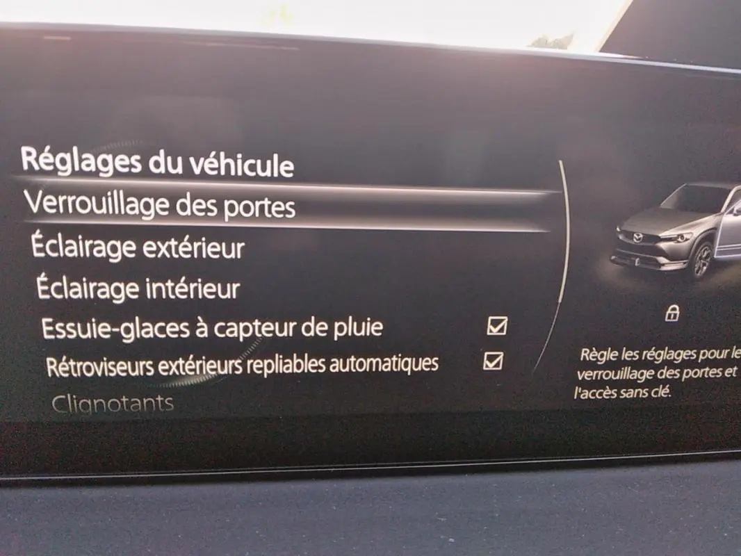 Écran intérieur du Mazda MX-30 2021 montrant les réglages de verrouillage des portes et options d'éclairage, avec illustration du véhicule gris.
