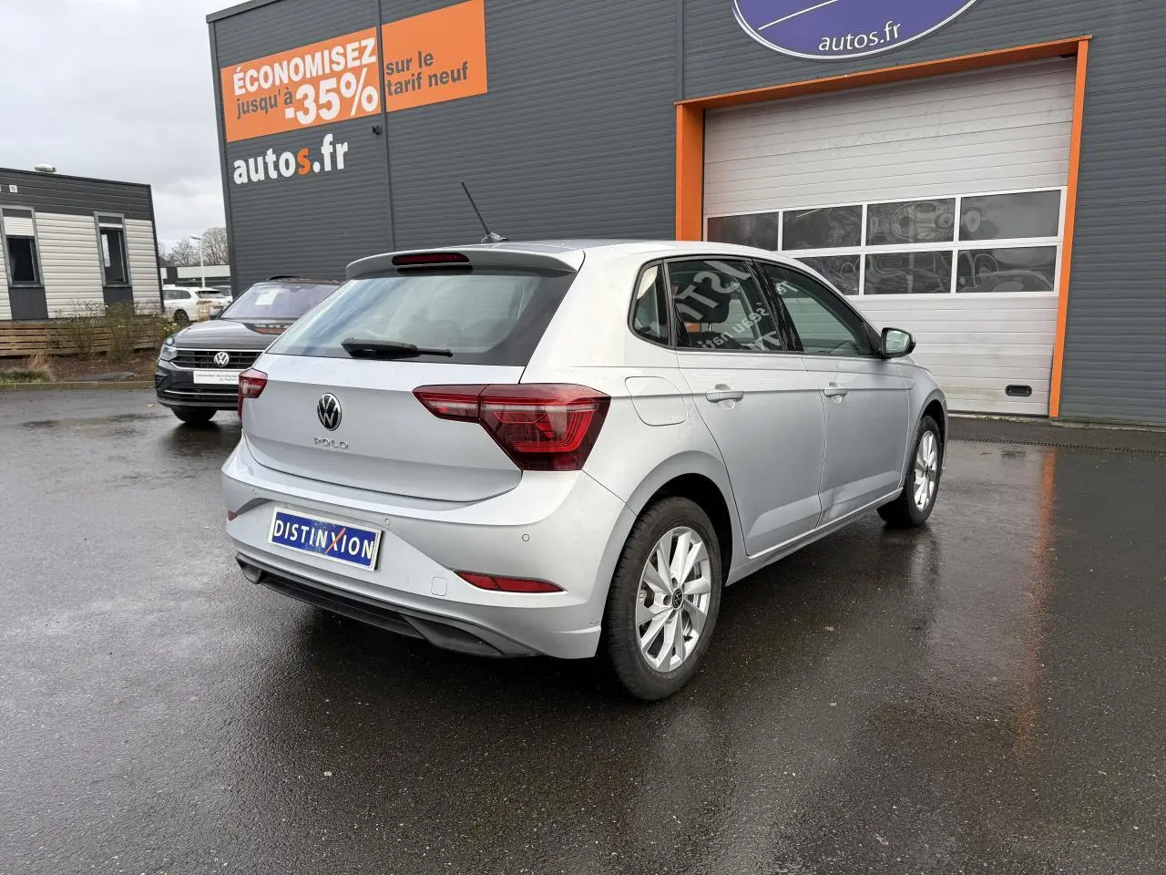 Volkswagen Polo 2025 couleur reflet d'argent métallisé vue 3/4 arrière droit sur parking humide devant un garage autos.fr