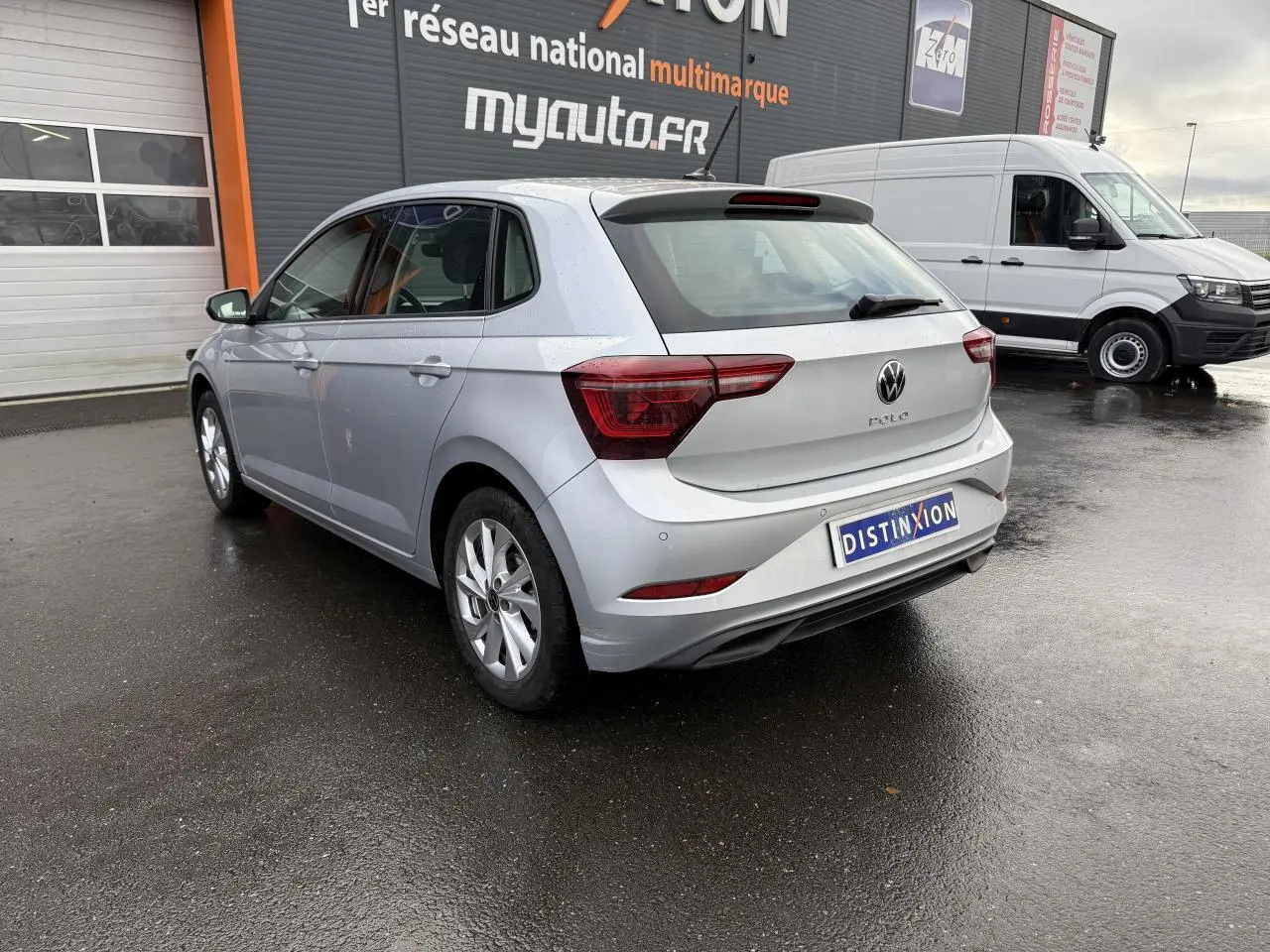 Volkswagen Polo 2025 argent métallisé vue 3/4 arrière droit sur sol mouillé devant un garage.