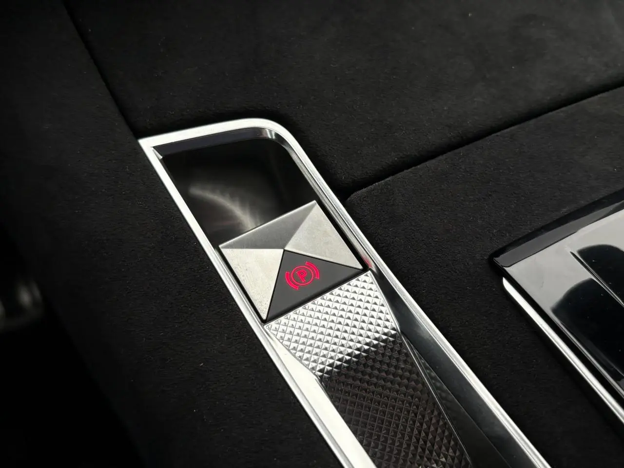 Gros plan sur le frein de stationnement électrique chromé dans la console centrale en Alcantara noir du DS7 gris laqué.