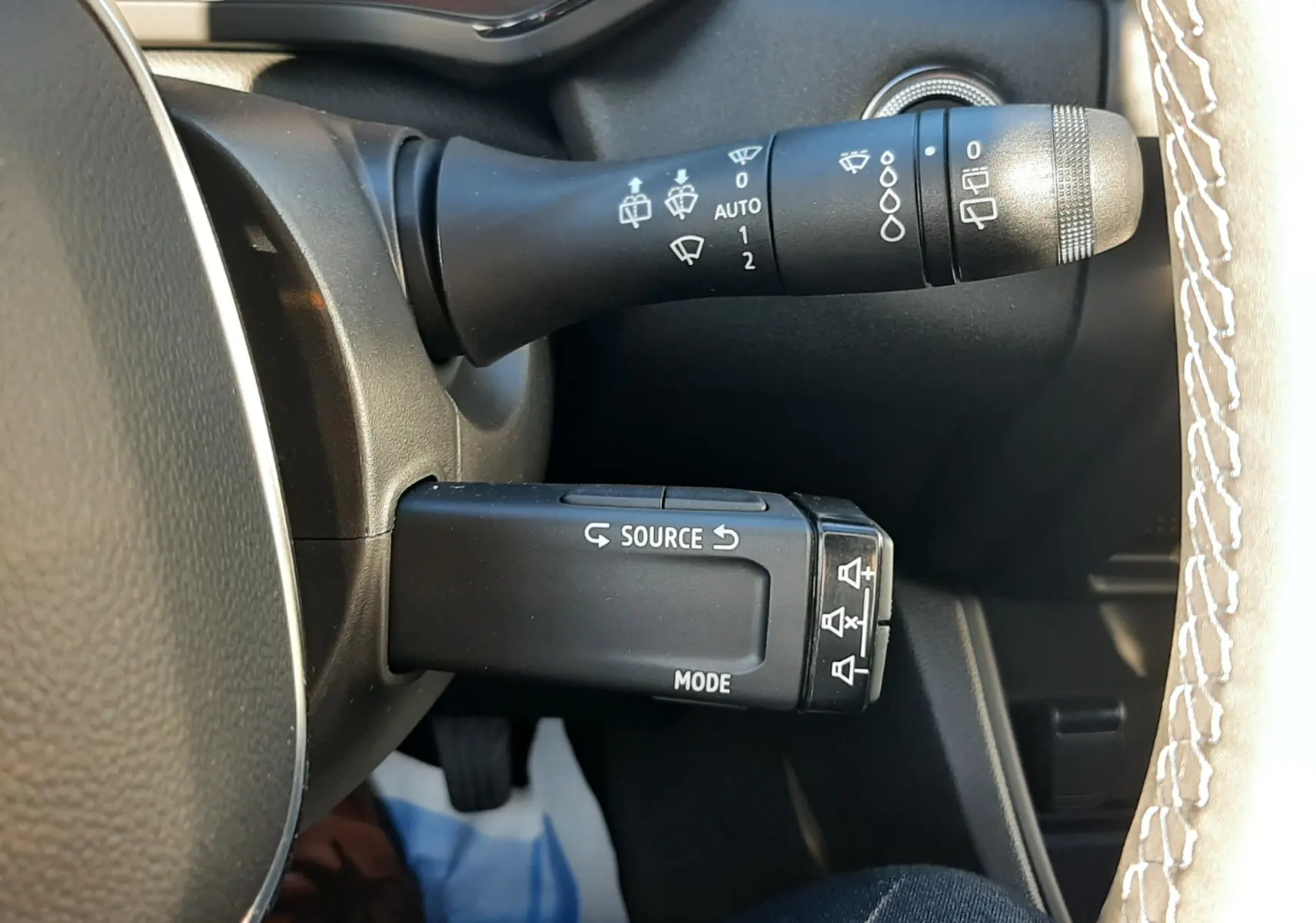 Gros plan sur les commandes au volant du Renault Captur II Ph.2, avec levier d'essuie-glace et boutons source et mode.
