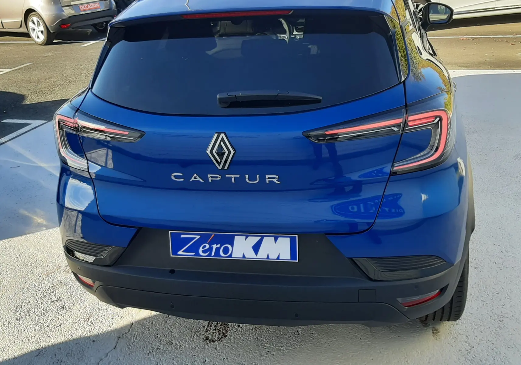 Vue arrière d'un Renault Captur bleu Iron 2025 avec feux LED et plaque d'immatriculation Zéro KM visible.