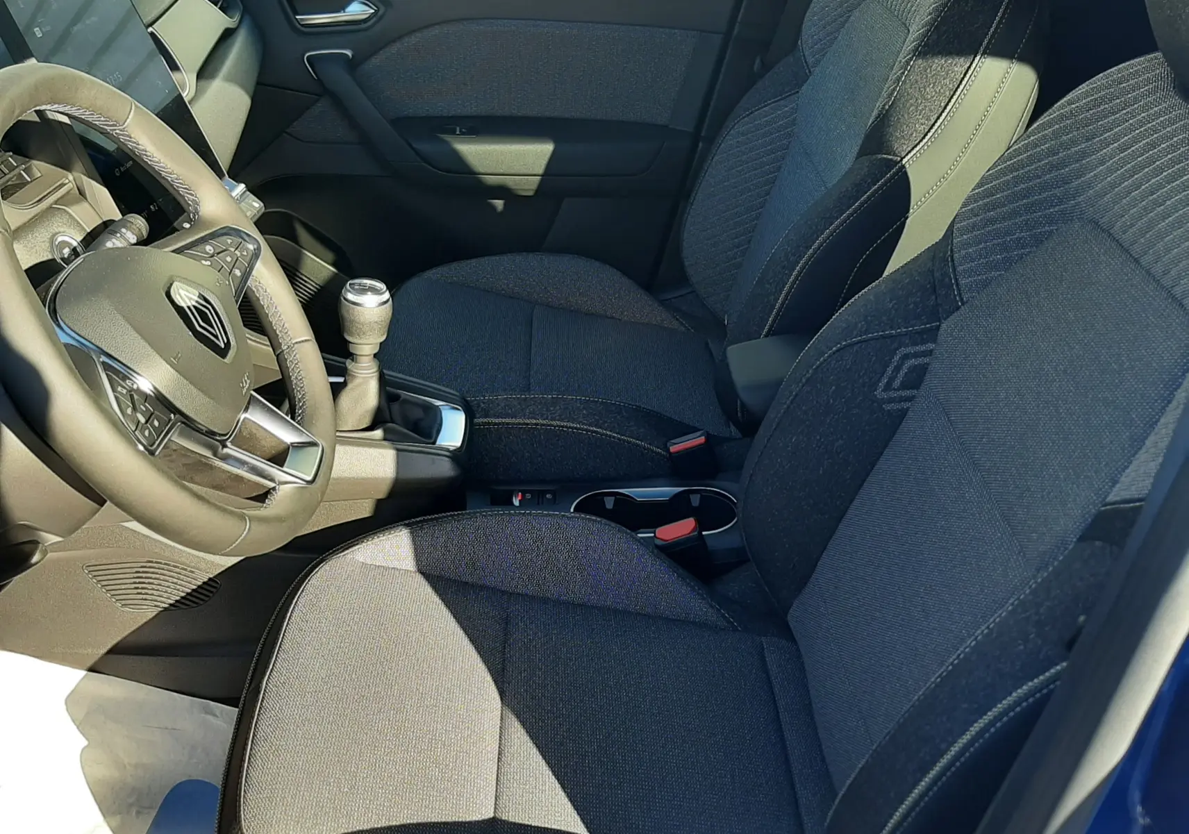 Intérieur côté conducteur du Renault Captur bleu Iron 2025, sièges tissu gris et volant multifonction visible.