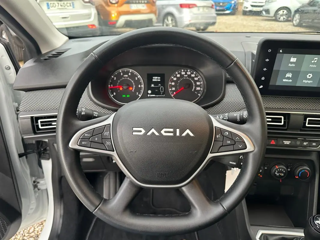 Vue intérieure centrée sur le volant noir de la Dacia Sandero 2024 avec tableau de bord et écran tactile visibles.