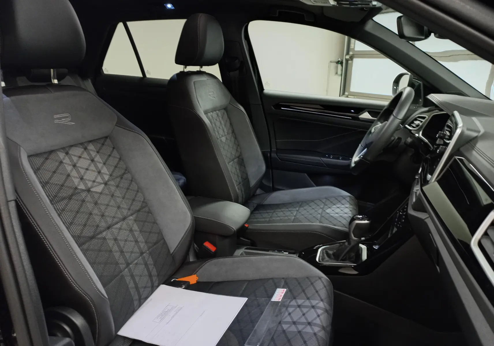 Vue intérieure côté droit du Volkswagen T-Roc 2025, sièges avant en tissu noir avec surpiqûres et logo R brodé.