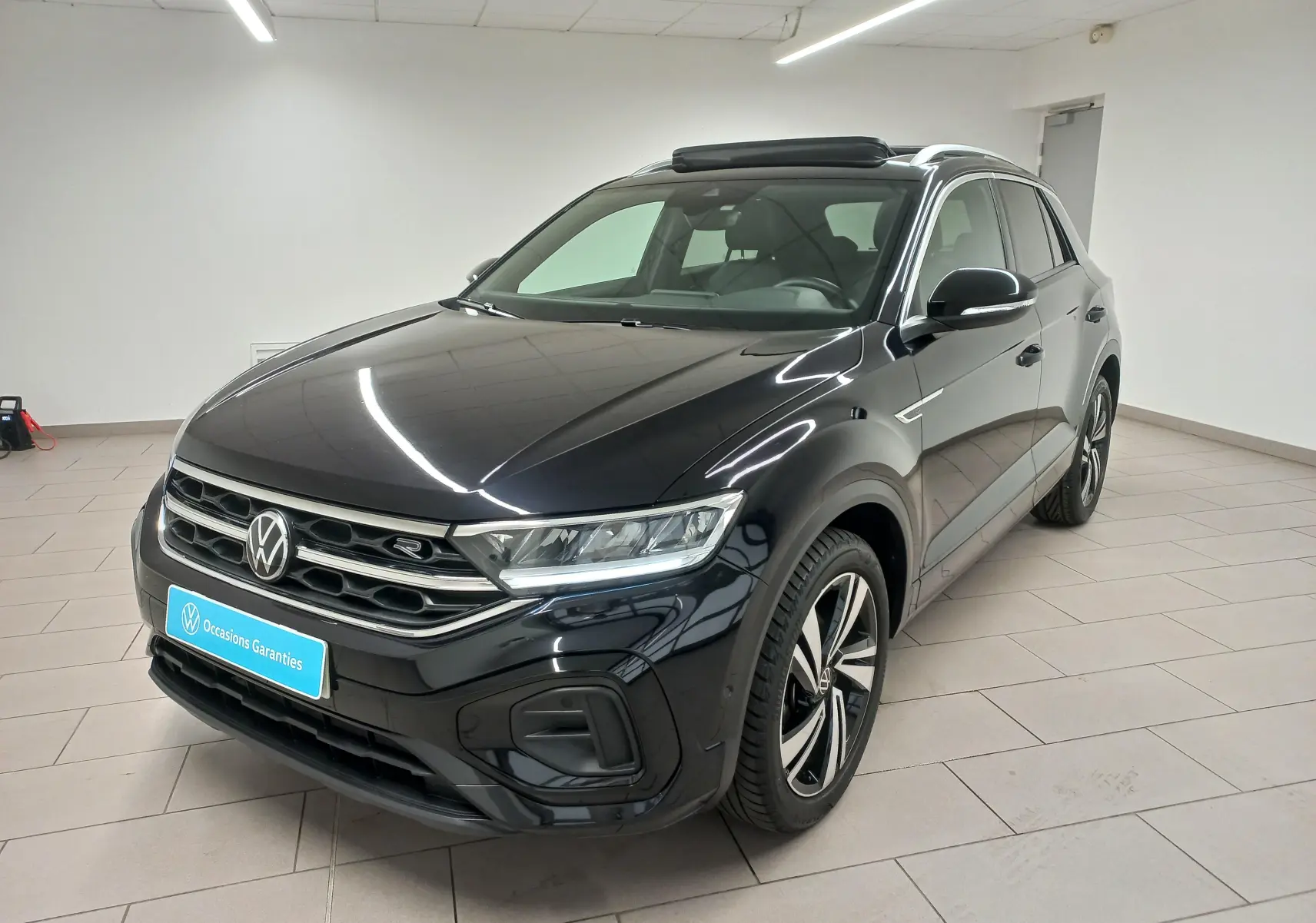Volkswagen T-Roc noir intense en vue 3/4 avant droit, avec toit ouvrant panoramique et jantes R-Line distinctives.