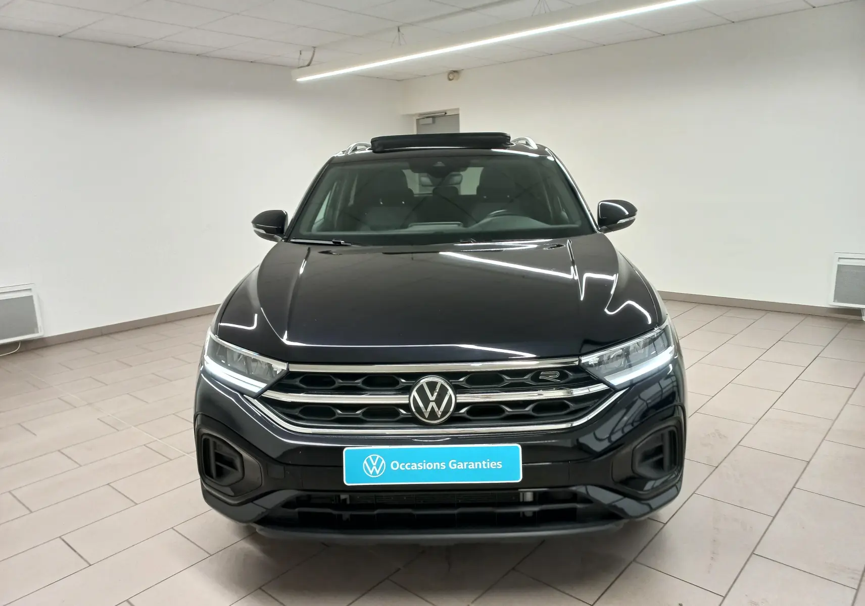 Vue frontale du Volkswagen T-Roc 1.5 TSI R-Line noir intense avec projecteurs LED allumés en intérieur showroom.