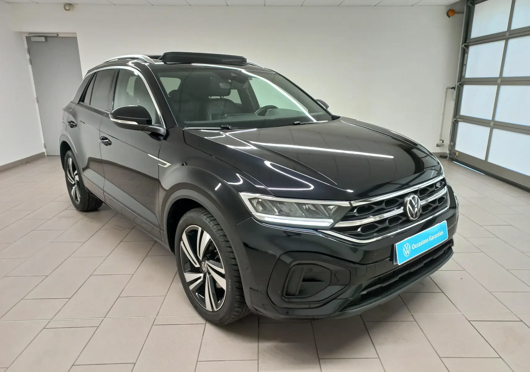 Vue 3/4 avant d’un Volkswagen T-Roc noir intense 2025 avec toit ouvrant panoramique et jantes R-Line distinctives.