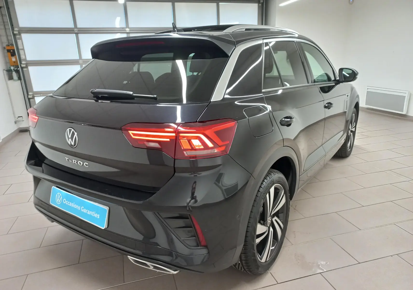 Vue 3/4 arrière droite du Volkswagen T-Roc noir intense, avec feux arrière LED allumés et jantes R-Line distinctives.