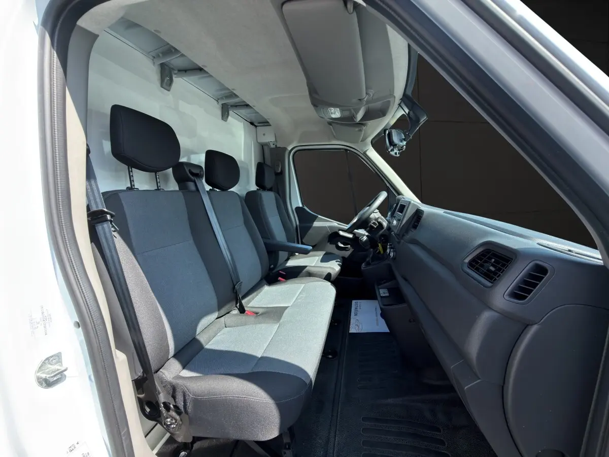 Vue intérieure côté conducteur du Renault Master 2024 blanc, montrant les sièges avant gris et le tableau de bord noir.