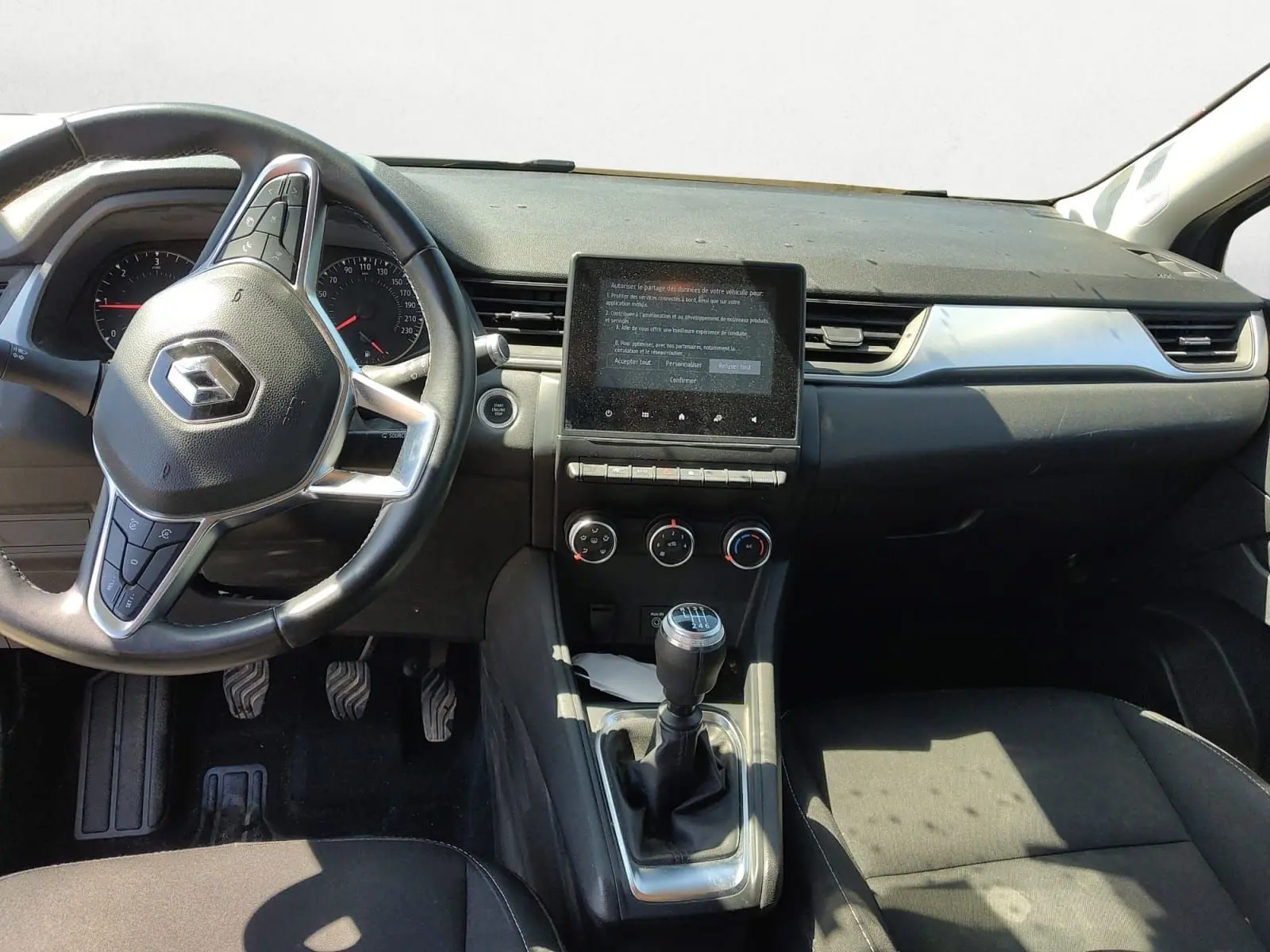 Vue intérieure avant du Renault Captur gris Cassiopée 2021, montrant le volant, la console centrale avec écran tactile et levier de vitesse manuel.