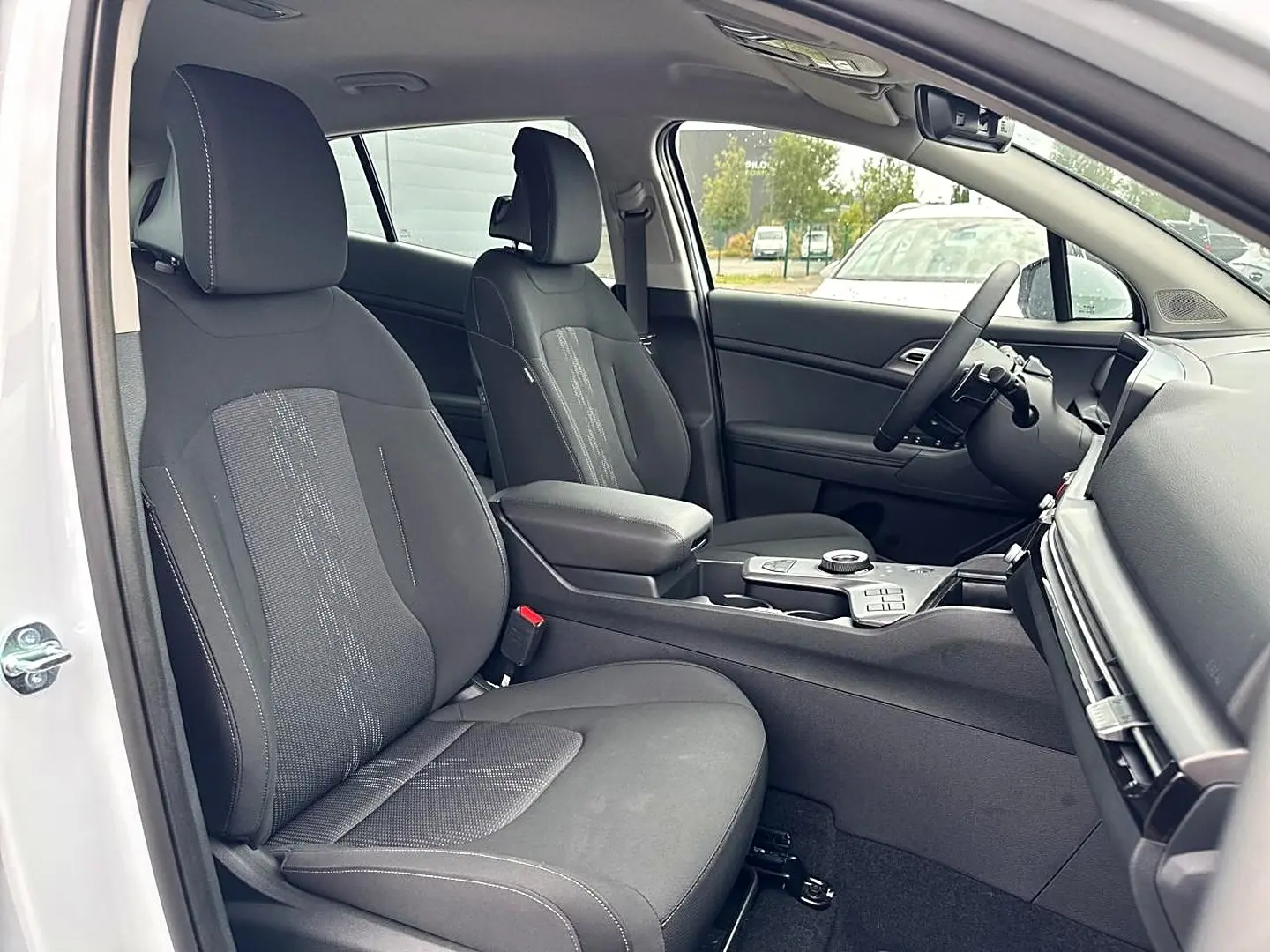 Vue intérieure côté conducteur du Kia Sportage blanc 2026, montrant les sièges avant noirs et la console centrale avec accoudoir.