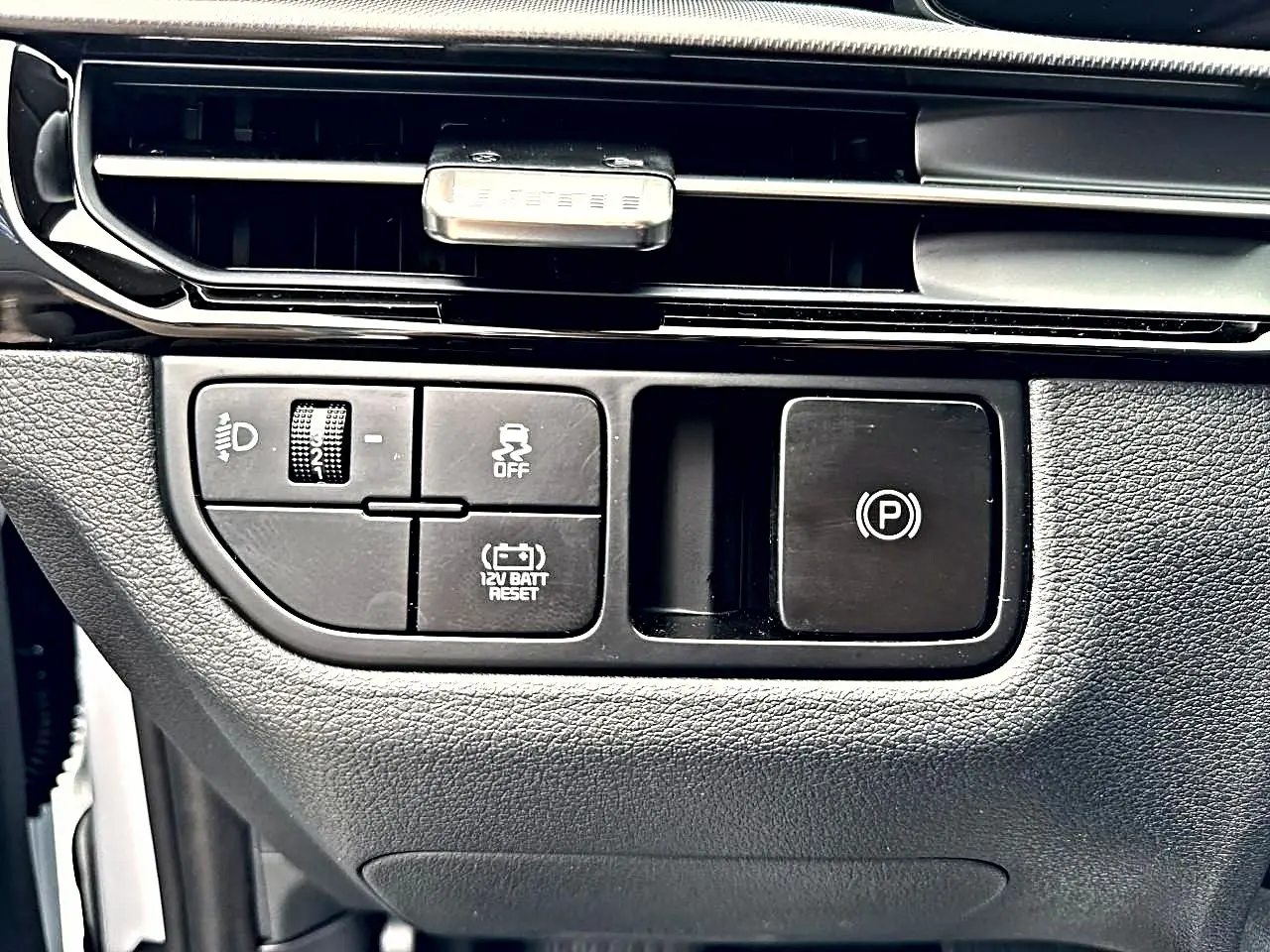 Gros plan sur les commandes noires du tableau de bord côté gauche du Kia Sportage blanc, avec bouton frein à main électronique.