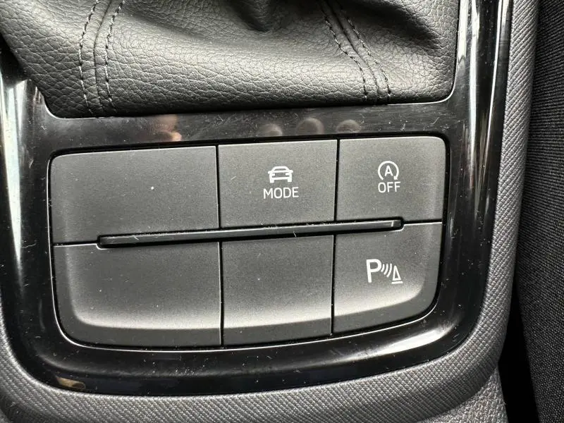 Gros plan sur les boutons de commande du mode de conduite et de l'aide au stationnement dans une Skoda Scala blanc cristal.