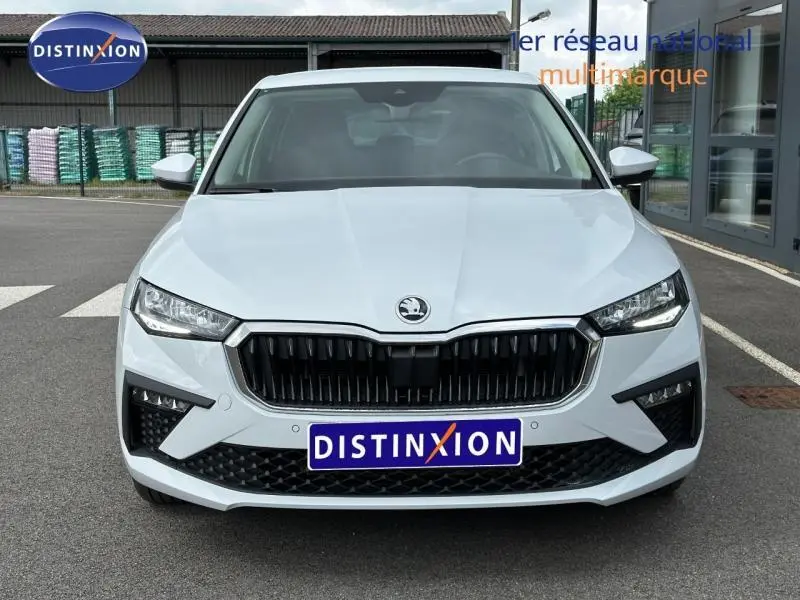 Vue frontale d'une Skoda Scala blanche Cristal avec calandre noire et phares LED, sur parking extérieur.