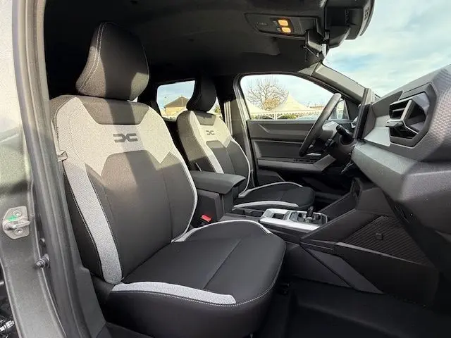 Vue intérieure côté conducteur du Dacia Duster 1.8 Hybrid 155 Journey 2026, sellerie spécifique gris et noir, tableau de bord moderne.