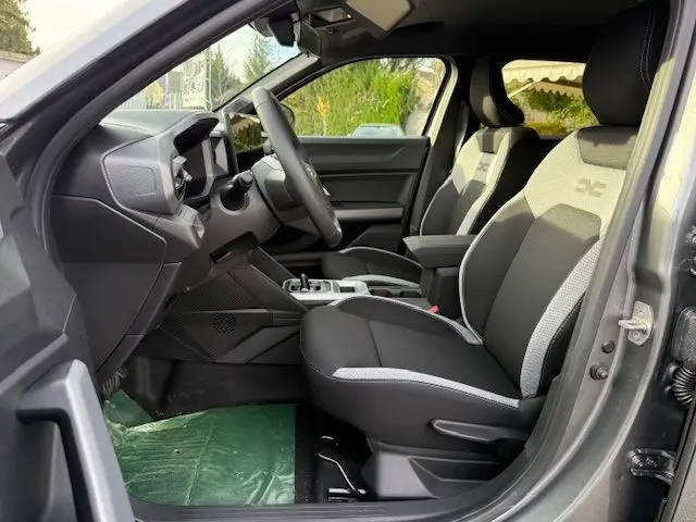 Vue intérieure côté conducteur du Dacia Duster 1.8 Hybrid 155 Journey avec sellerie spécifique gris et noir, tableau de bord moderne.