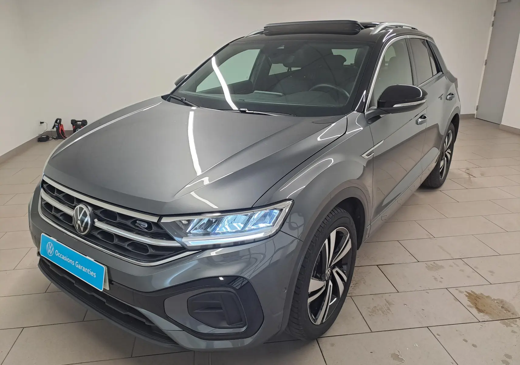 Volkswagen T-Roc 2025 gris Indium avec toit noir, vue 3/4 avant mettant en valeur les phares LED Matrix et jantes R-Line.