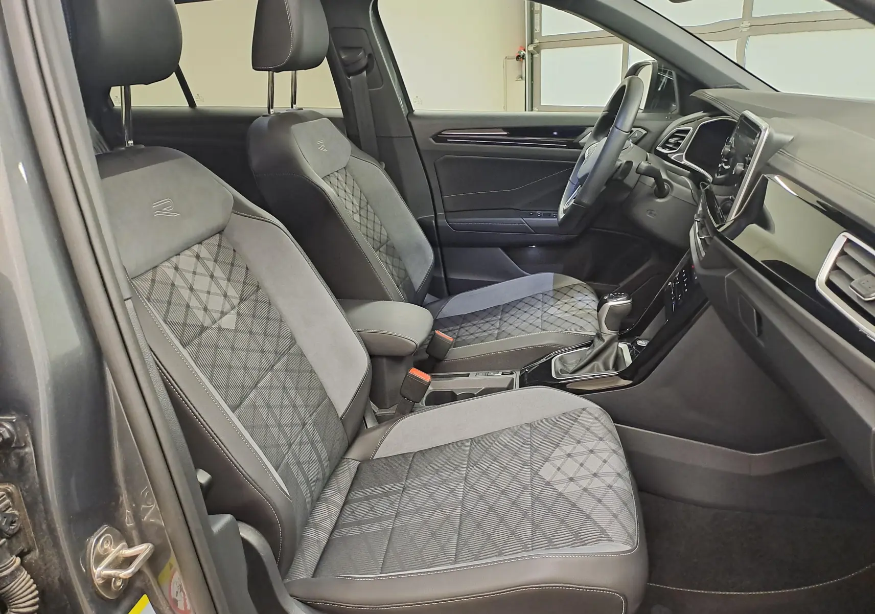 Vue intérieure côté conducteur du Volkswagen T-Roc 1.5 TSI R-Line 2025, sièges tissu et alcantara gris avec surpiqûres.