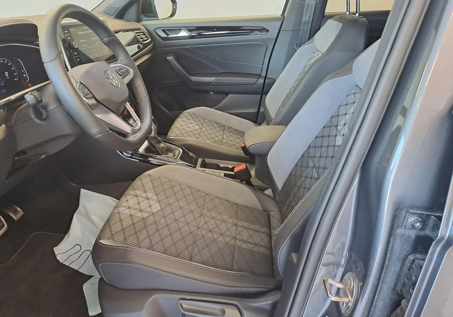 Vue intérieure côté conducteur du Volkswagen T-Roc 2025 gris Indium, sièges tissu et cuir avec motifs géométriques.