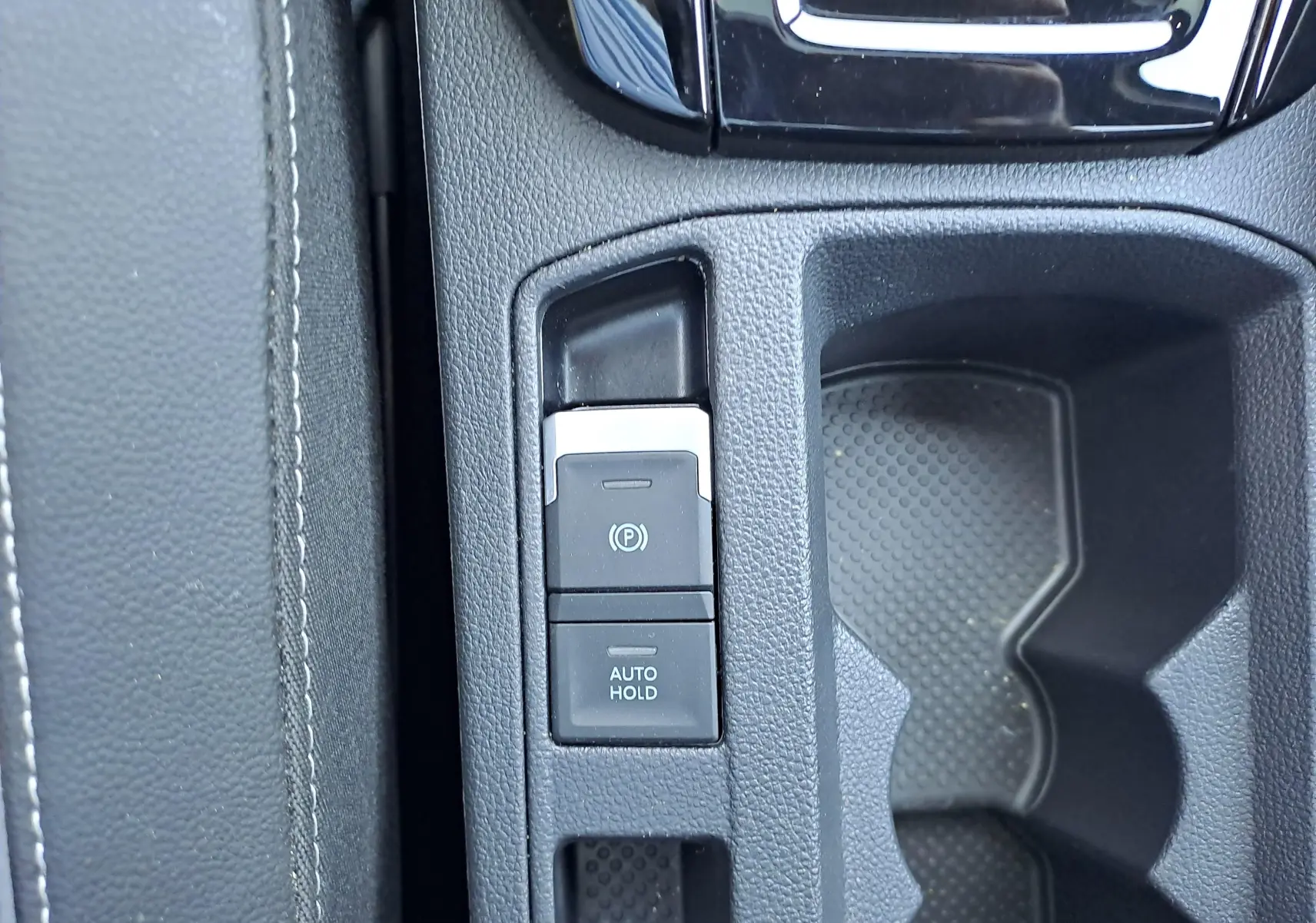 Gros plan sur la console centrale du Volkswagen T-Roc 2025, boutons de frein à main électrique et auto hold visibles.