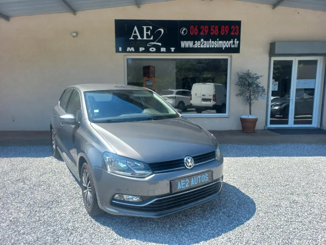 Volkswagen Polo gris vue 3/4 avant droit, avec calandre noire et jantes alliage, stationnée devant un commerce.