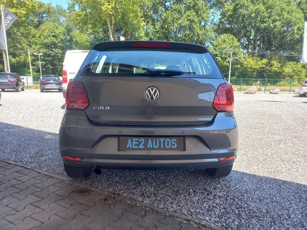 Vue arrière d'une Volkswagen Polo gris 2016, avec feux rouges et plaque AE2 AUTOS visible sur un parking extérieur.