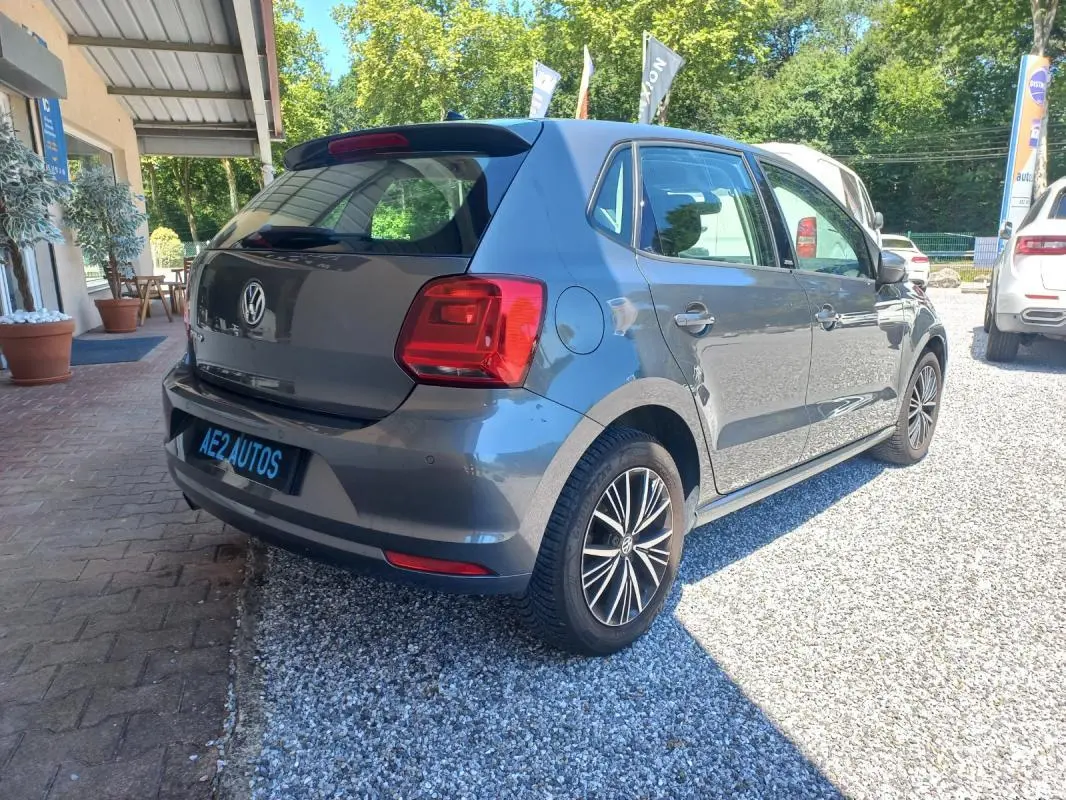 Volkswagen Polo gris vue 3/4 arrière droit, avec jantes alliage et feux arrière distinctifs, stationnée sur gravier.
