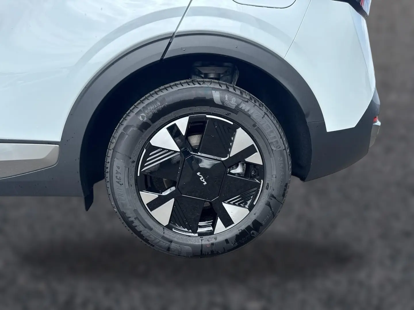 Gros plan sur la roue arrière droite du KIA Sportage blanc 2026 avec jante alu noire et argentée au design moderne.