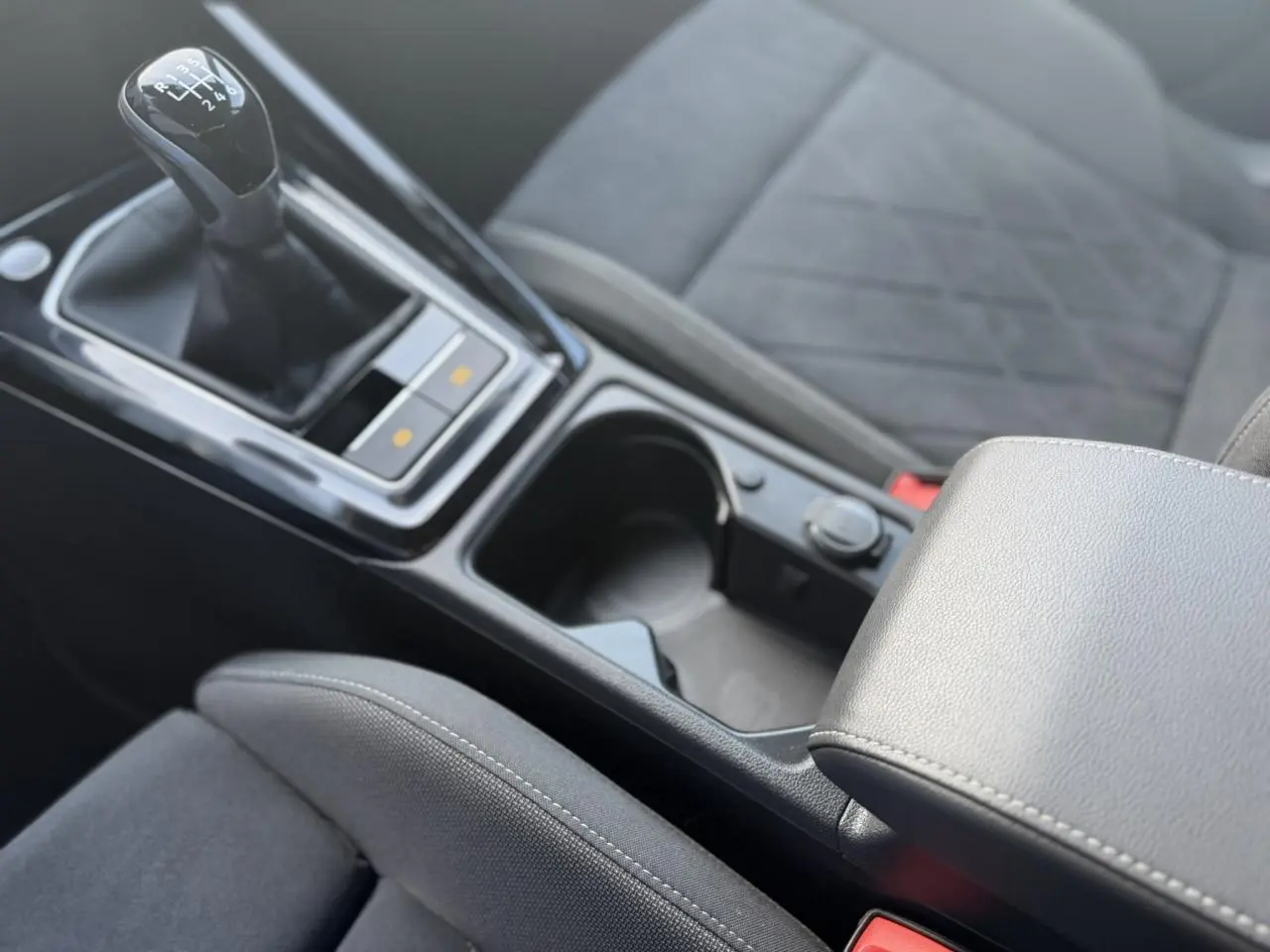 Gros plan intérieur sur la console centrale et levier de vitesses manuel de la Volkswagen Golf VIII 1.5 TSI noir avec accoudoir réglable.