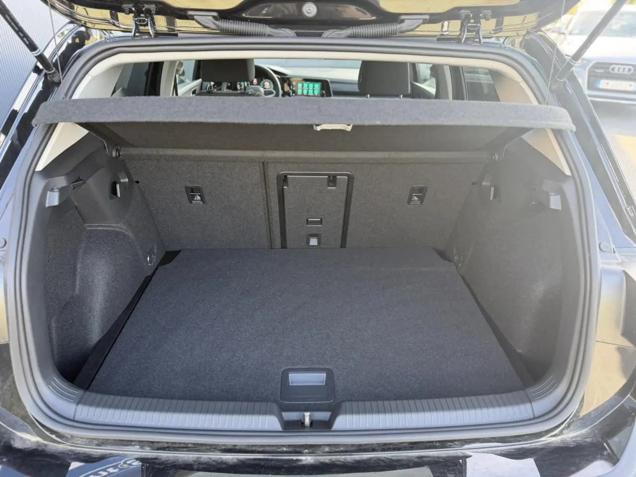Coffre ouvert vu de l'arrière d'une Volkswagen Golf VIII noire, montrant un espace de chargement propre et spacieux.