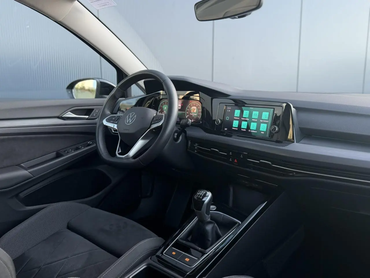 Intérieur de la Volkswagen Golf VIII 2024, vue côté conducteur, tableau de bord numérique et levier de vitesses manuel noir.