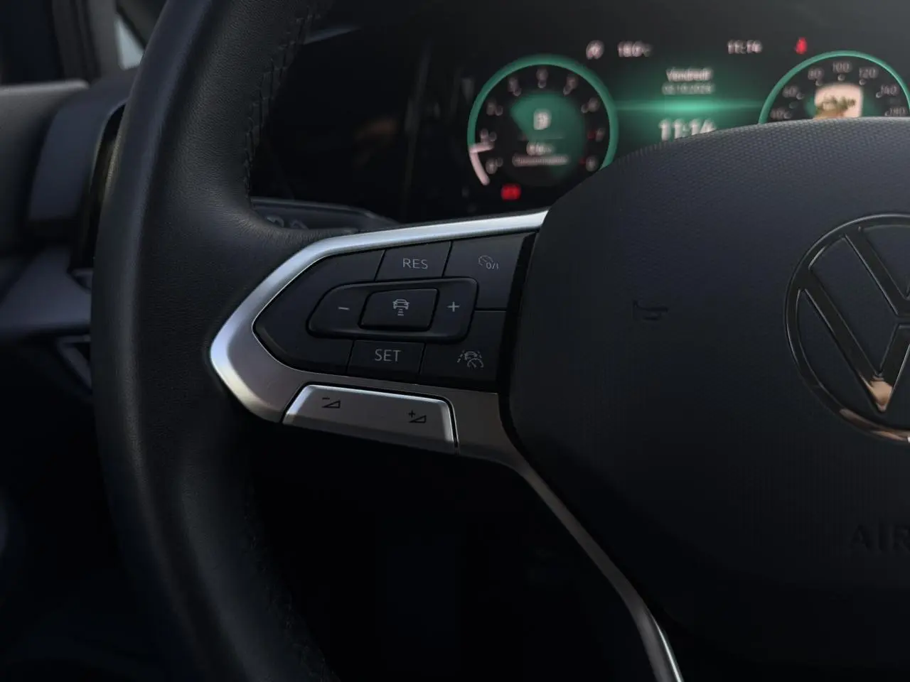 Gros plan sur le volant cuir noir de la Volkswagen Golf VIII 2024, avec commandes multifonctions et tableau de bord numérique en arrière-plan.