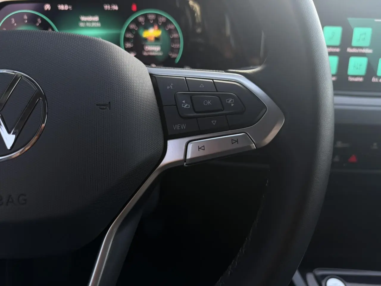 Gros plan sur le volant multifonction noir de la Volkswagen Golf VIII 2024 avec commandes et tableau de bord numérique en arrière-plan.