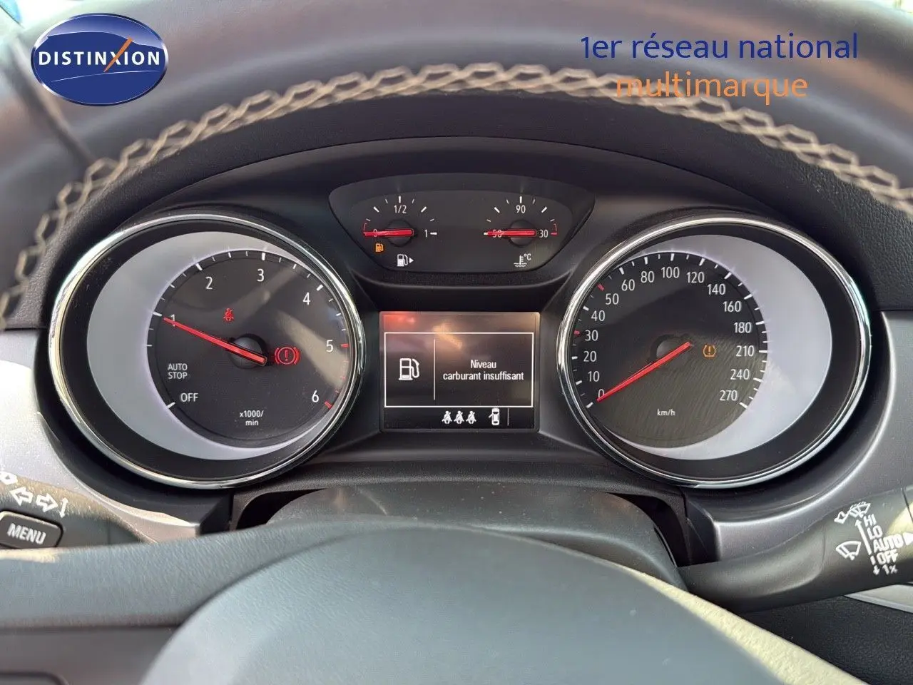 Vue rapprochée du tableau de bord de l'Opel Astra Sports Tourer gris minéral, affichant un avertissement de carburant faible.