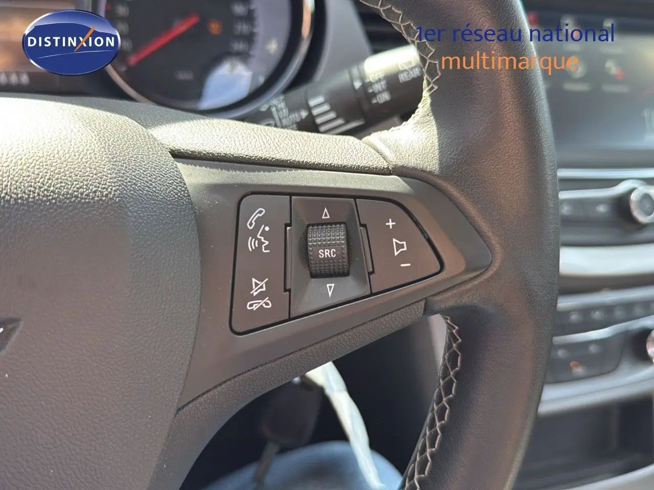 Gros plan sur les commandes au volant en cuir noir de l'Opel Astra Sports Tourer gris minéral, tableau de bord en arrière-plan.