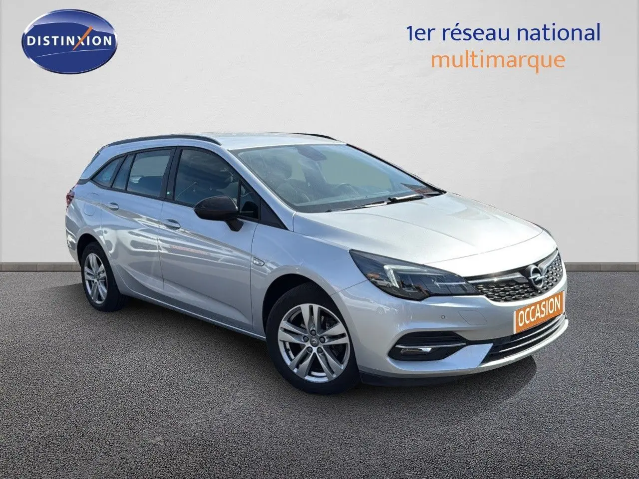 Opel Astra Sports Tourer gris minéral métal vue 3/4 avant droit avec calandre noire et jantes alliage.