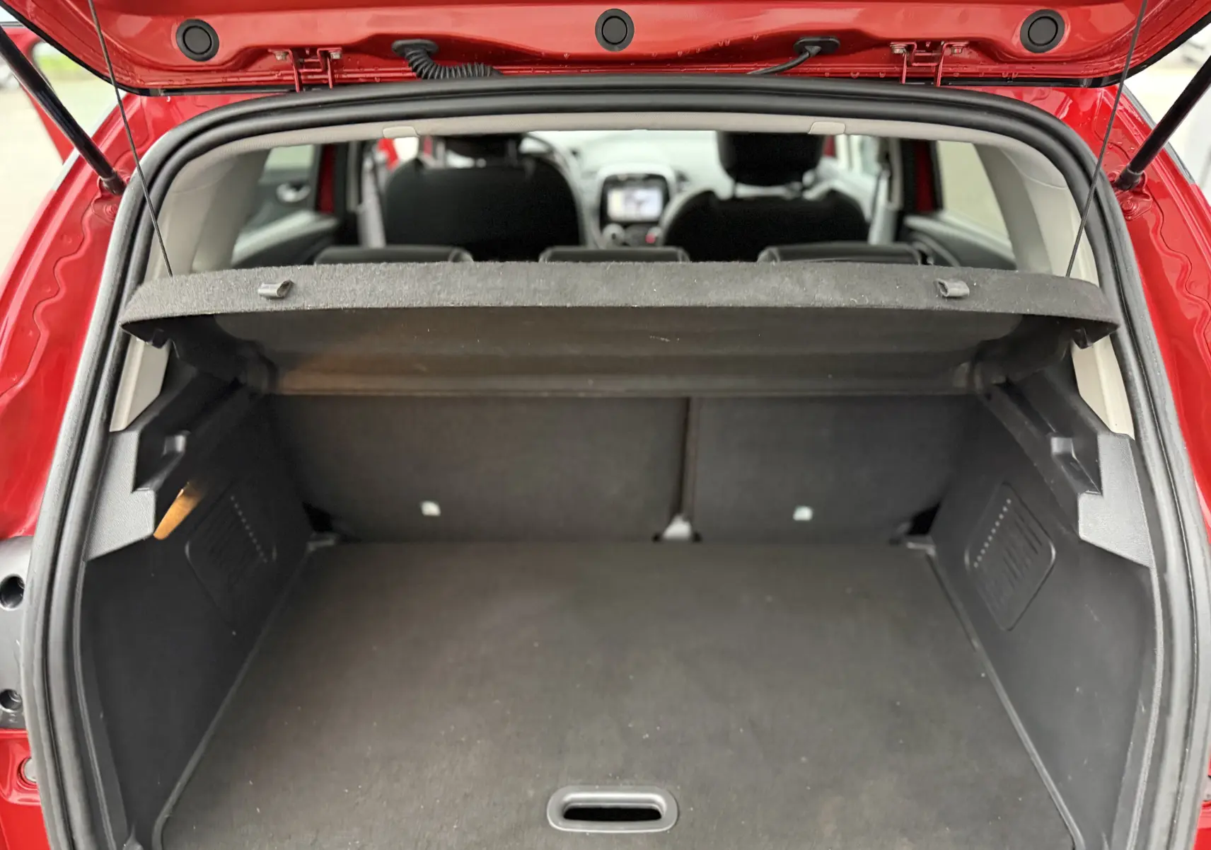Coffre ouvert vu de l'arrière d'un Renault Captur rouge, montrant l'espace de chargement et l'intérieur noir.