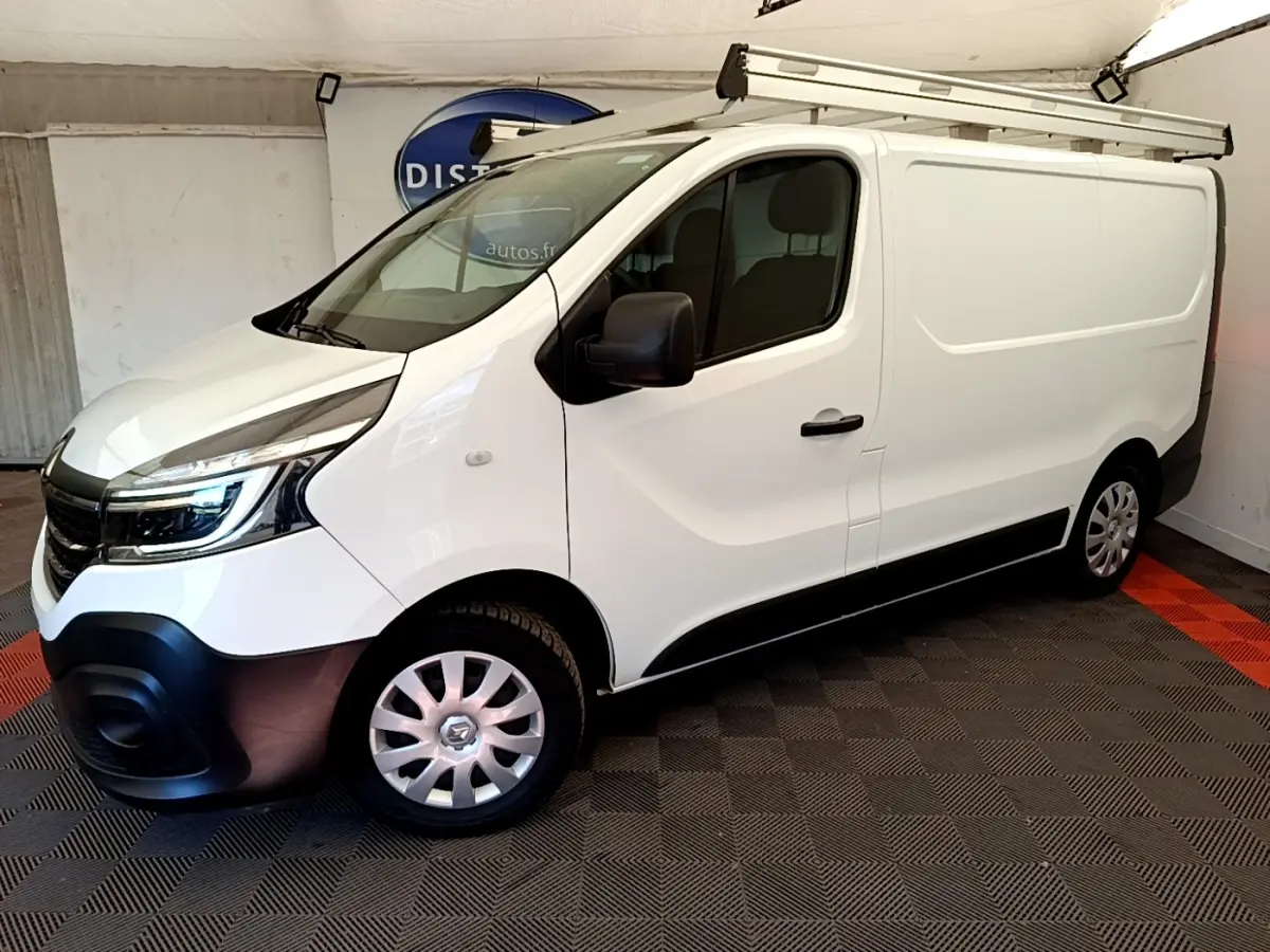 Renault Trafic Fourgon blanc en vue 3/4 avant droit, avec galerie de toit et jantes acier argentées.