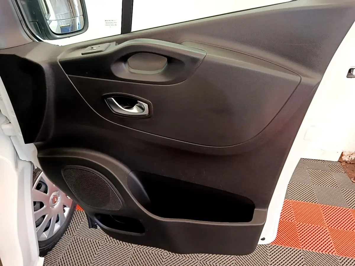 Vue rapprochée de la porte avant gauche noire du Renault Trafic Fourgon blanc, avec poignée et haut-parleur intégrés.