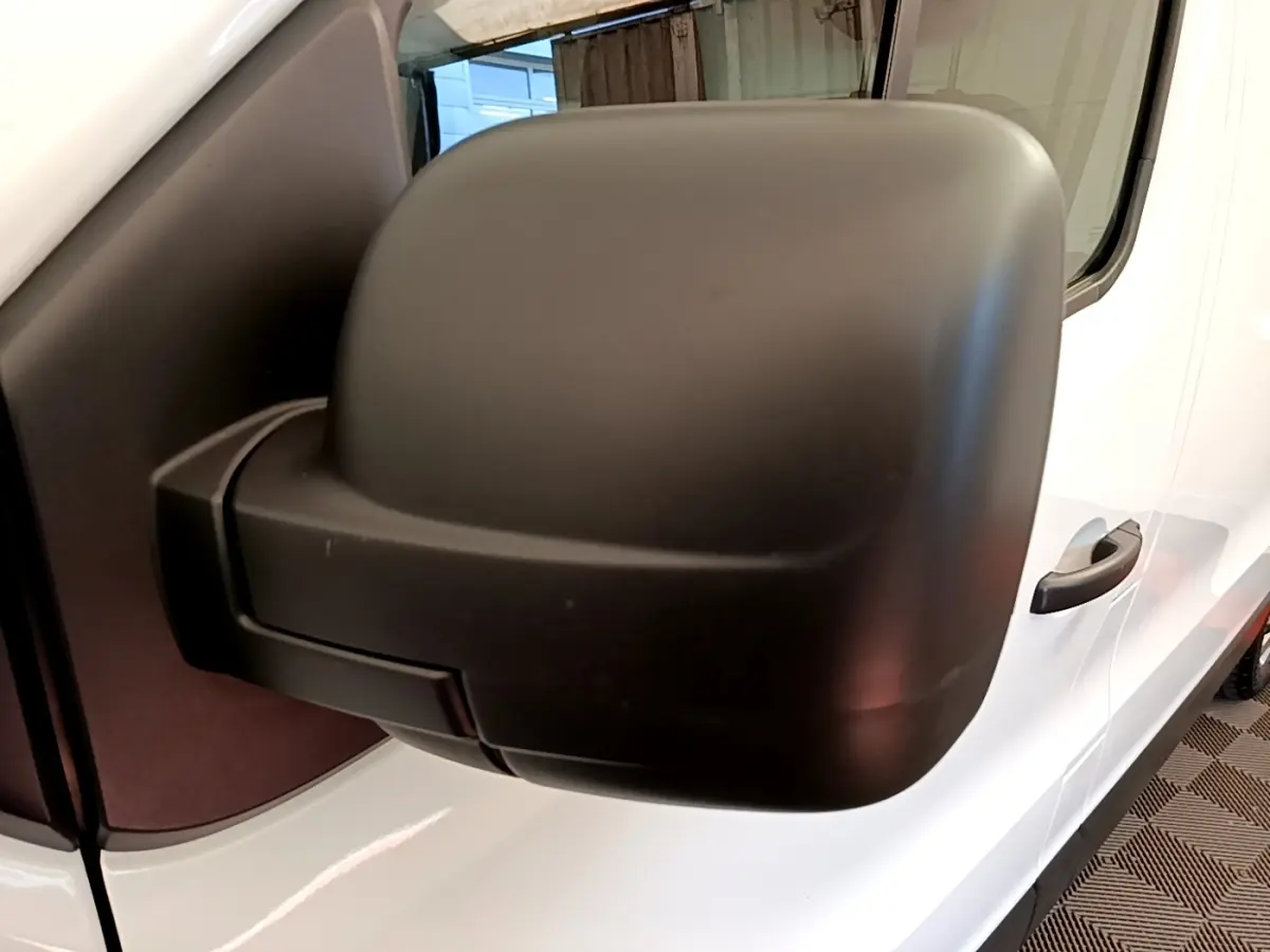Gros plan sur le rétroviseur noir côté conducteur du Renault Trafic Fourgon blanc, vue latérale droite.