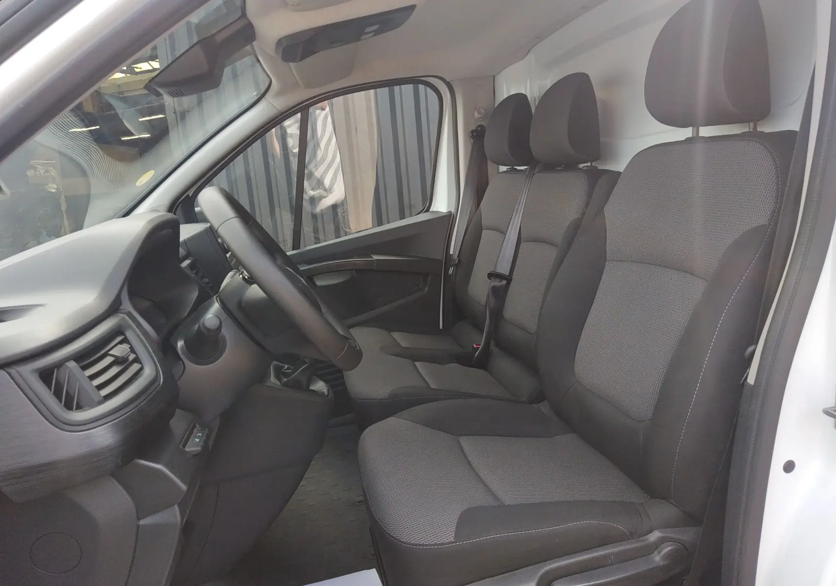 Vue intérieure côté conducteur du Renault Trafic Fourgon blanc 2024, montrant les sièges tissu gris et le volant multifonction.