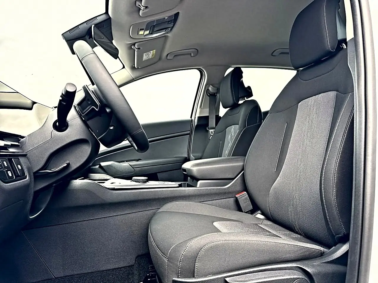 Vue intérieure côté conducteur du Kia Sportage hybride 2026, sièges noirs et accoudoir central avec rangement visible.