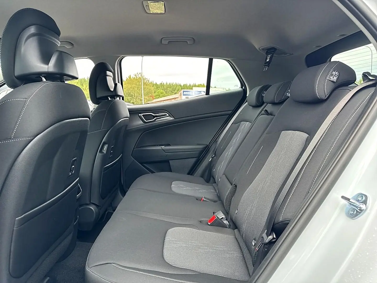 Vue intérieure côté droit montrant la banquette arrière grise et les dossiers des sièges avant d’un KIA Sportage blanc.